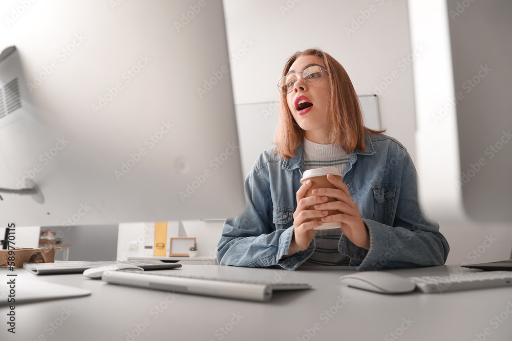 Surprised female programmer with cup of coffee working at table in office