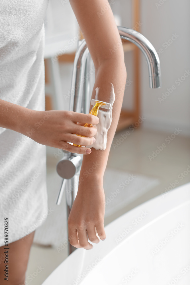 Young woman shaving her arm with razor in bathroom, closeup