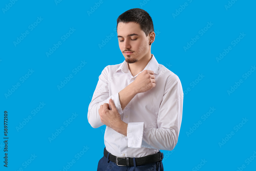 Young businessman rolling up his sleeve on light blue background