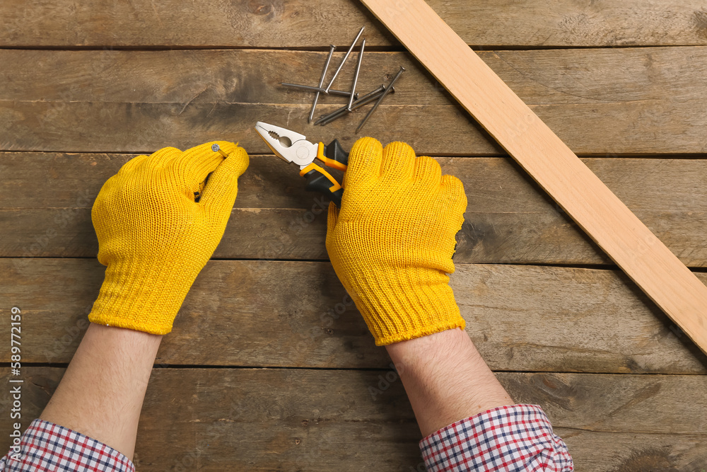 Man holding pliers and nail near wooden table