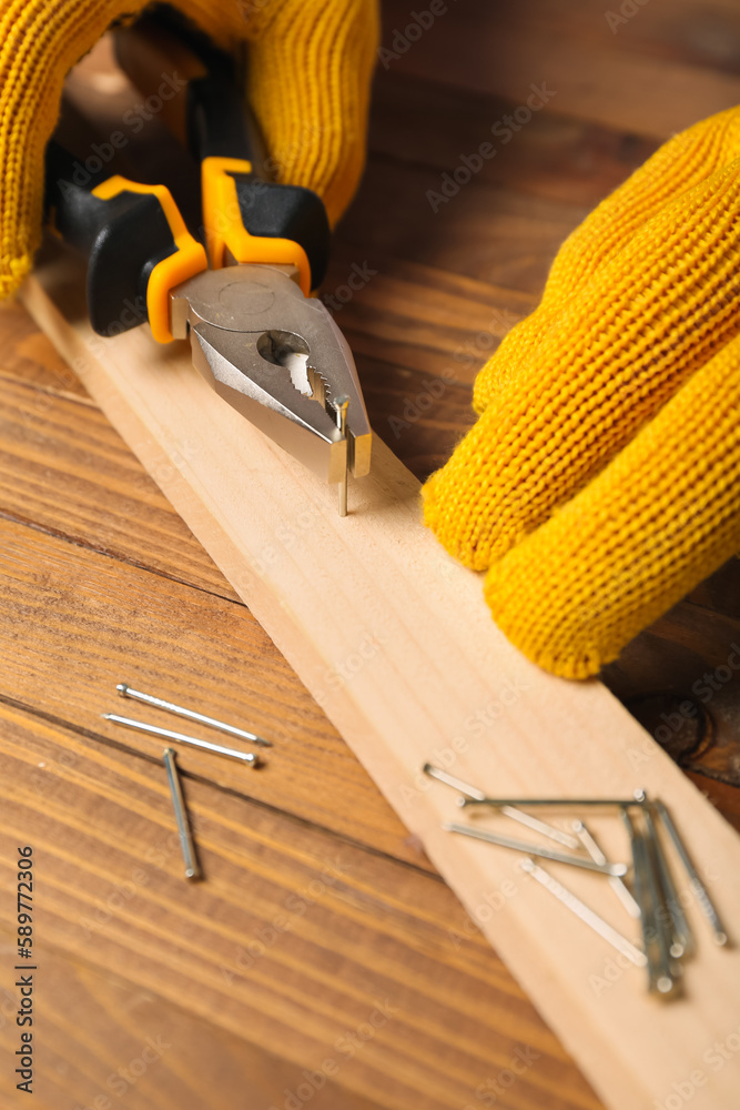 Man with pliers pulling nail out from wooden plank on table