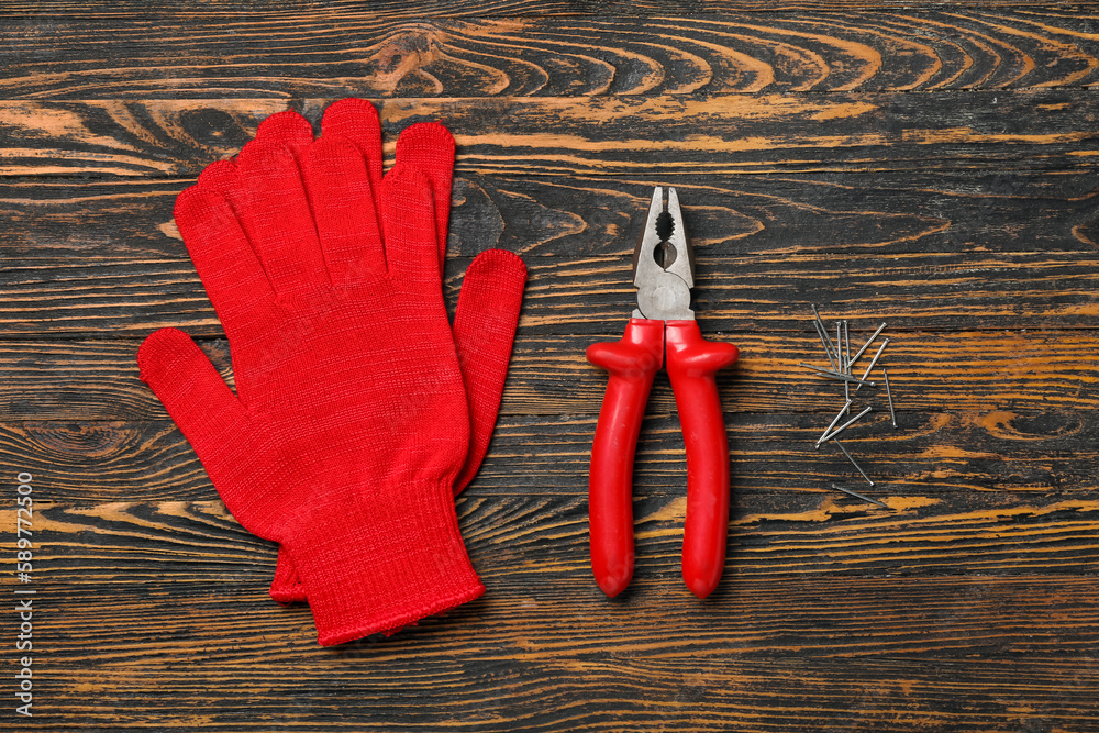 Pliers, gloves and nails on wooden background