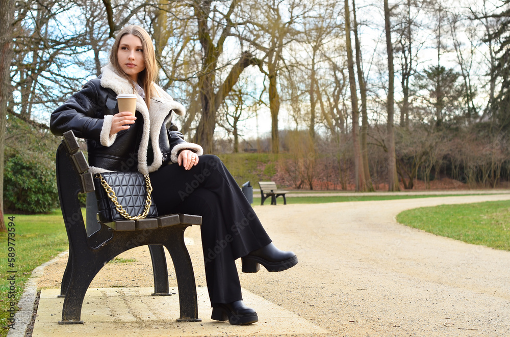 Young woman with cup of coffee sitting on bench in park