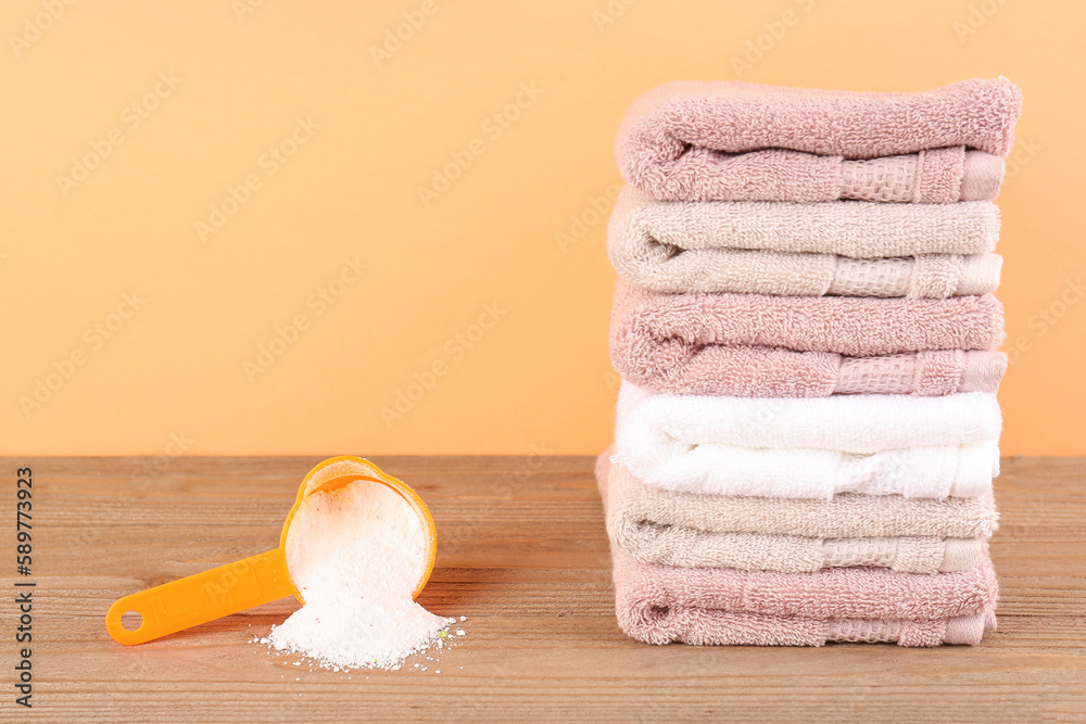 Laundry detergent and folded towels on wooden table against orange background