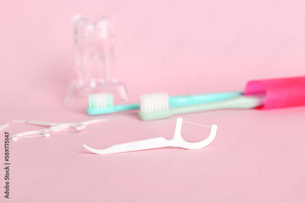 Floss toothpicks, brushes and plastic tooth model on pink background