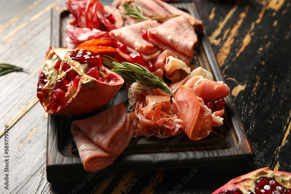 Board with assortment of tasty deli meats on dark wooden background, closeup