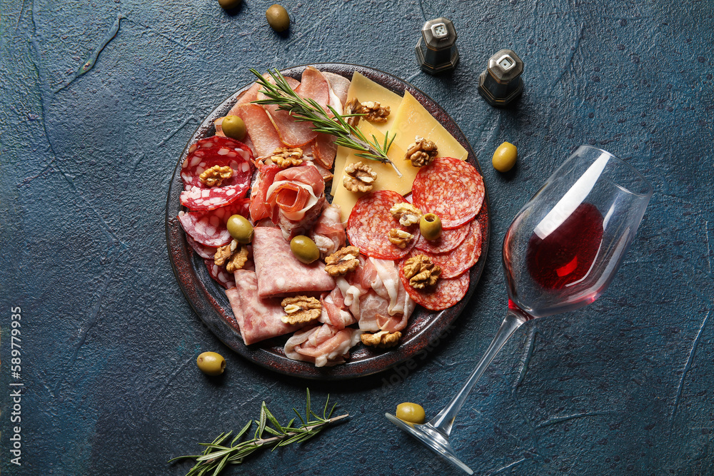 Plate with assortment of tasty deli meats, cheese and wine glass on black background