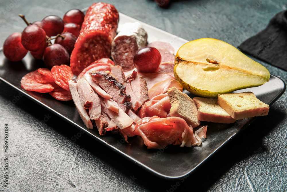 Plate with assortment of tasty deli meats on black background, closeup