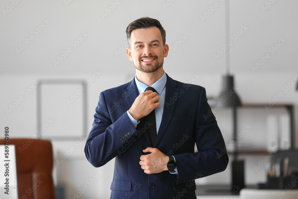 Handsome businessman fixing his necktie in office