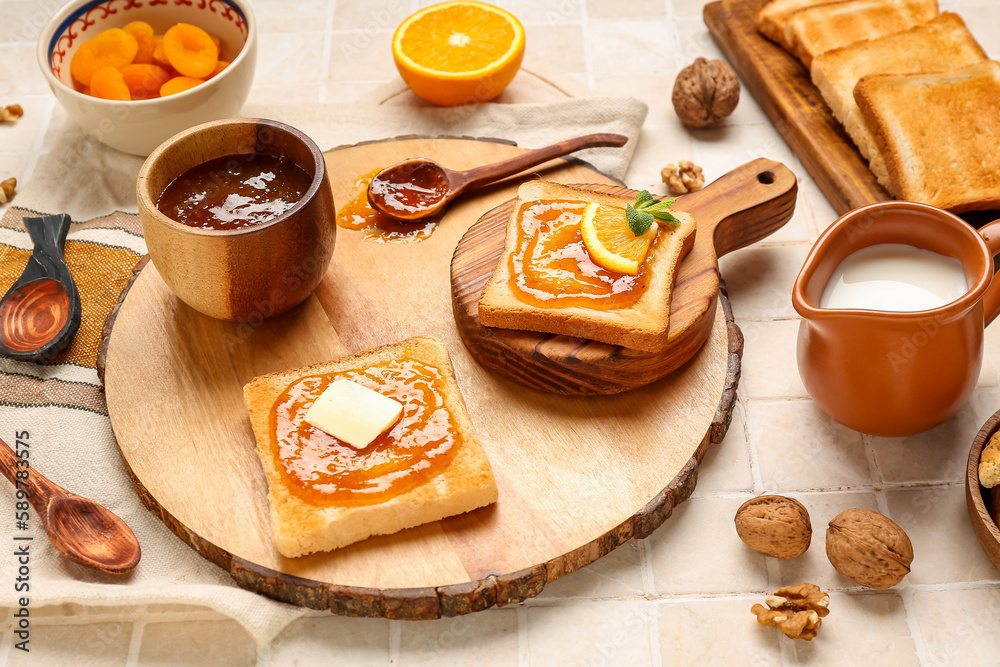 Wooden boards of tasty toasts with apricot jam on light tile background