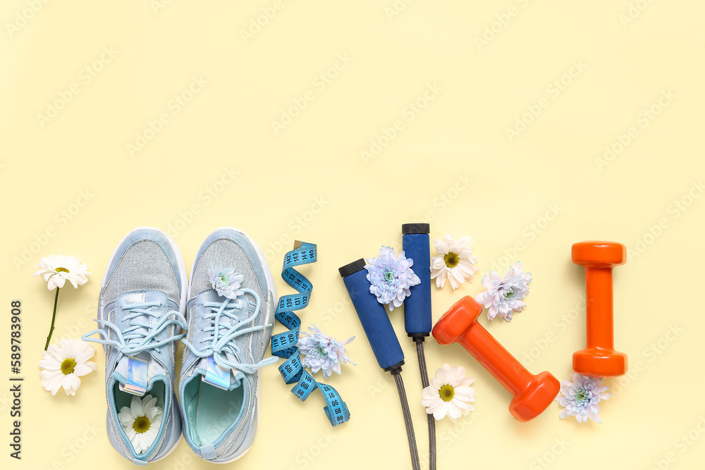 Sneakers with spring flowers, sports equipment and tape measure on beige background