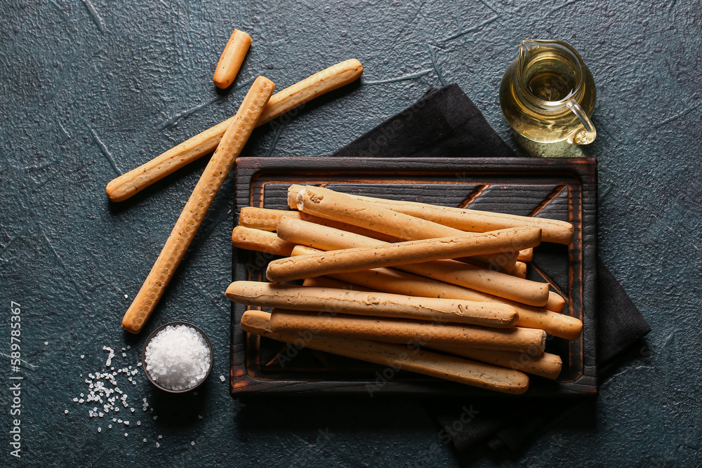 Wooden board with tasty Italian Grissini on dark background