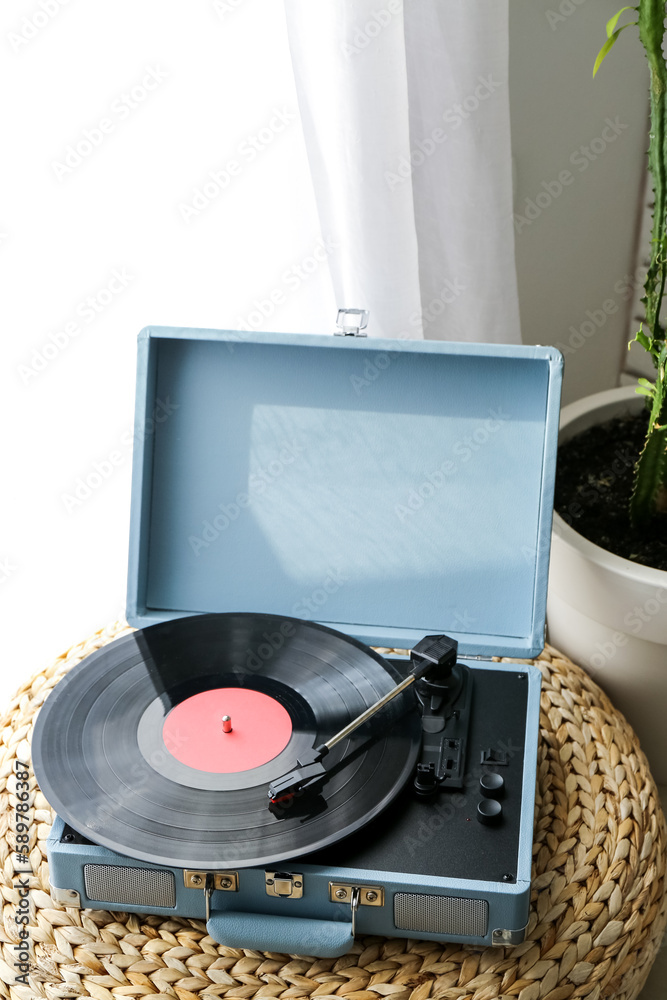 Record player with vinyl disk on pouf in room