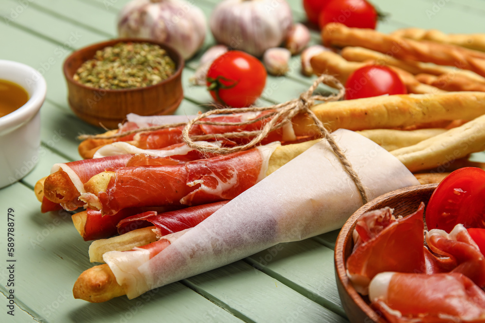 Bunch of tasty Italian Grissini with bacon on green wooden background, closeup