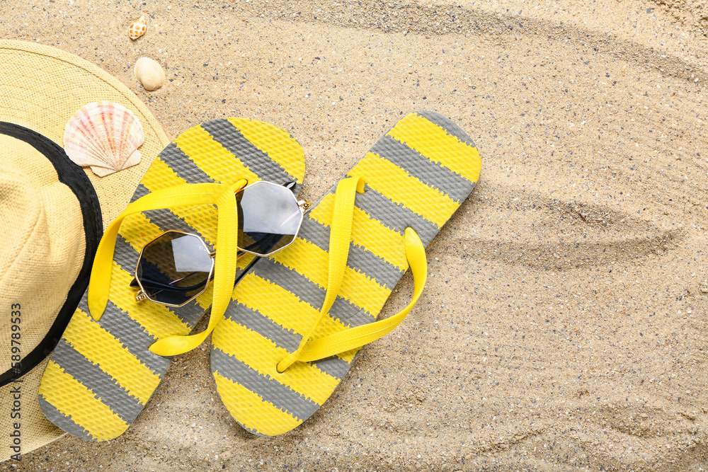 Flip-flops with sunglasses, hat and seashells on sand