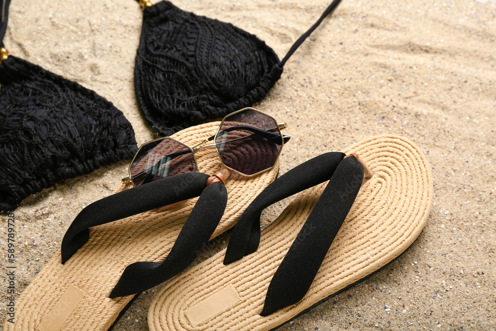 Flip-flops with sunglasses and swimsuit on sand, closeup