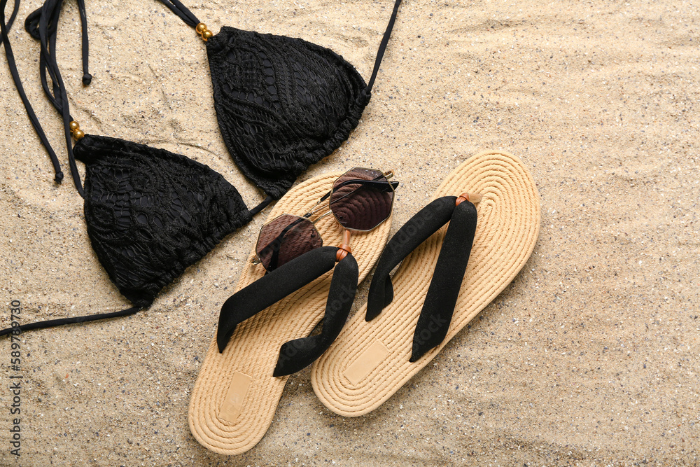 Flip-flops with sunglasses and swimsuit on sand