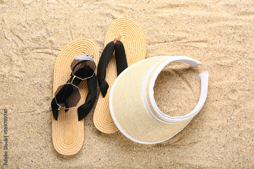 Flip-flops with sunglasses and cap on sand