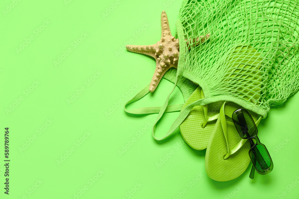 String bag with flip-flops, sunglasses and starfish on green background