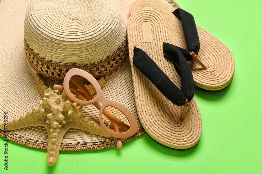 Flip-flops with sunglasses, starfish and hat on green background, closeup