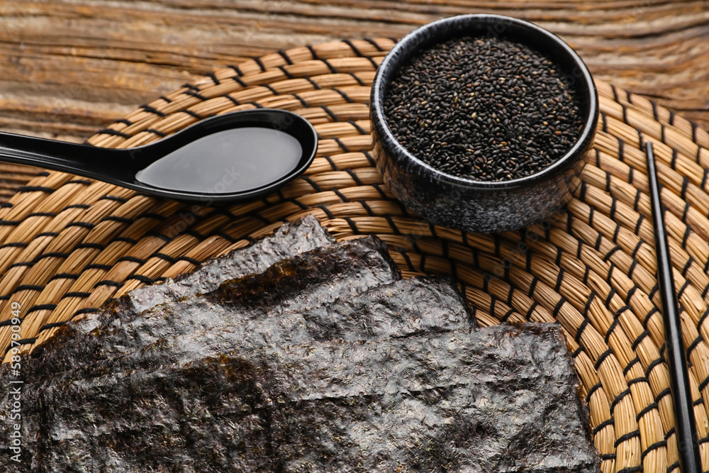 Wicker mat with nori sheets, sesame seeds and sauce on wooden background, closeup