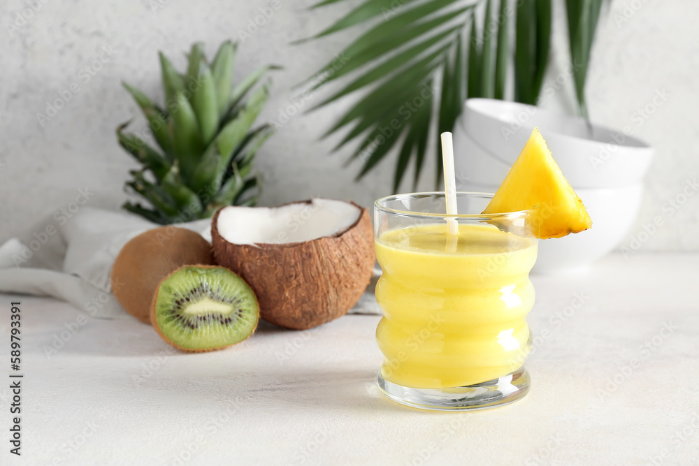 Glass of tasty pineapple smoothie, kiwi and coconut on table