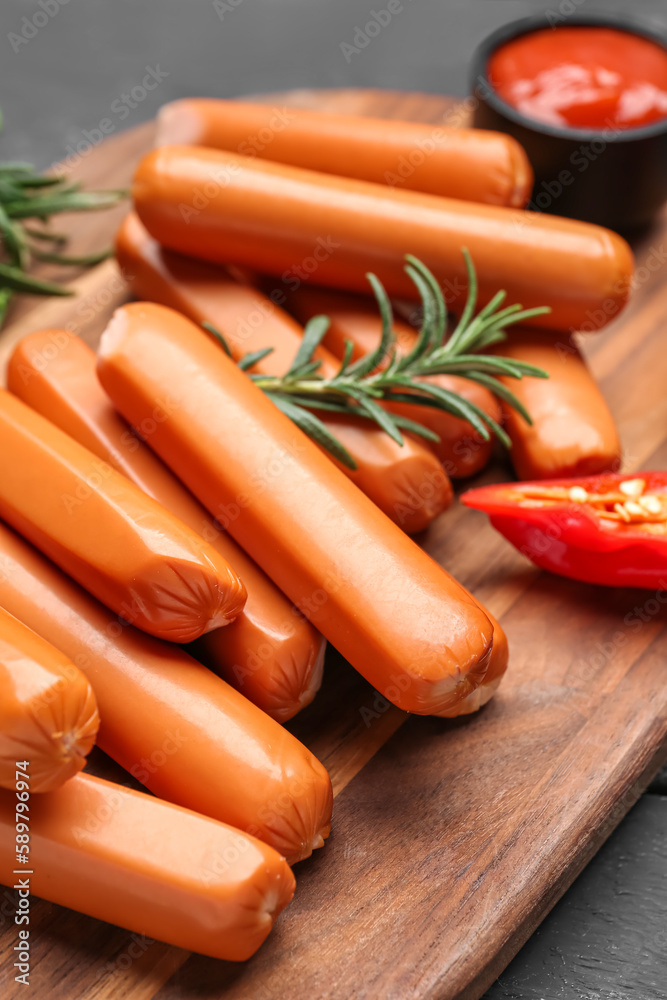 Wooden board with tasty sausages on table