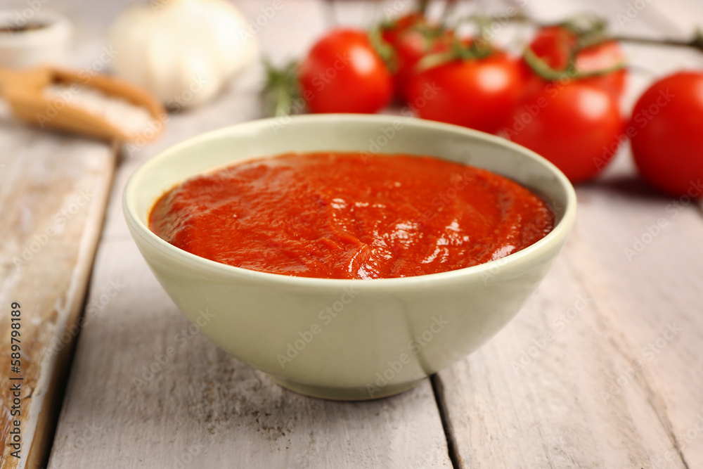 Bowl with tasty tomato paste on light wooden background, closeup