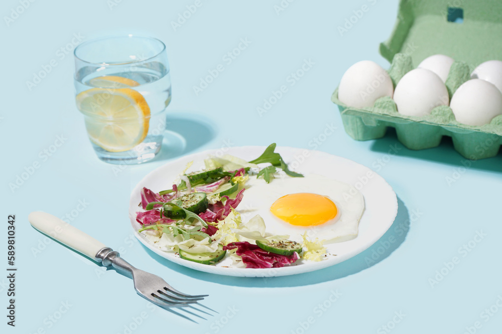 Plate with tasty fried egg and salad on blue background