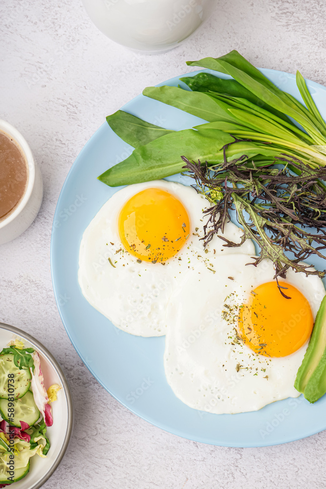 Plate with tasty fried eggs, coffee and greens on light table