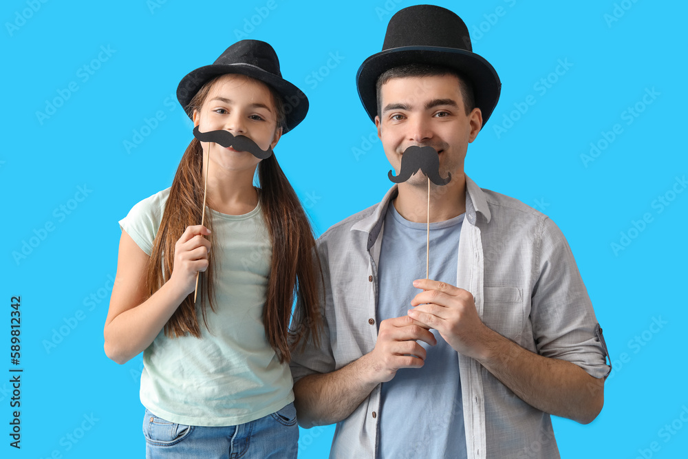 Portrait of father and his little daughter with paper mustache on light blue background