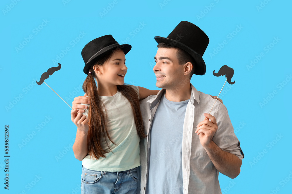 Portrait of father and his little daughter with paper mustache on light blue background