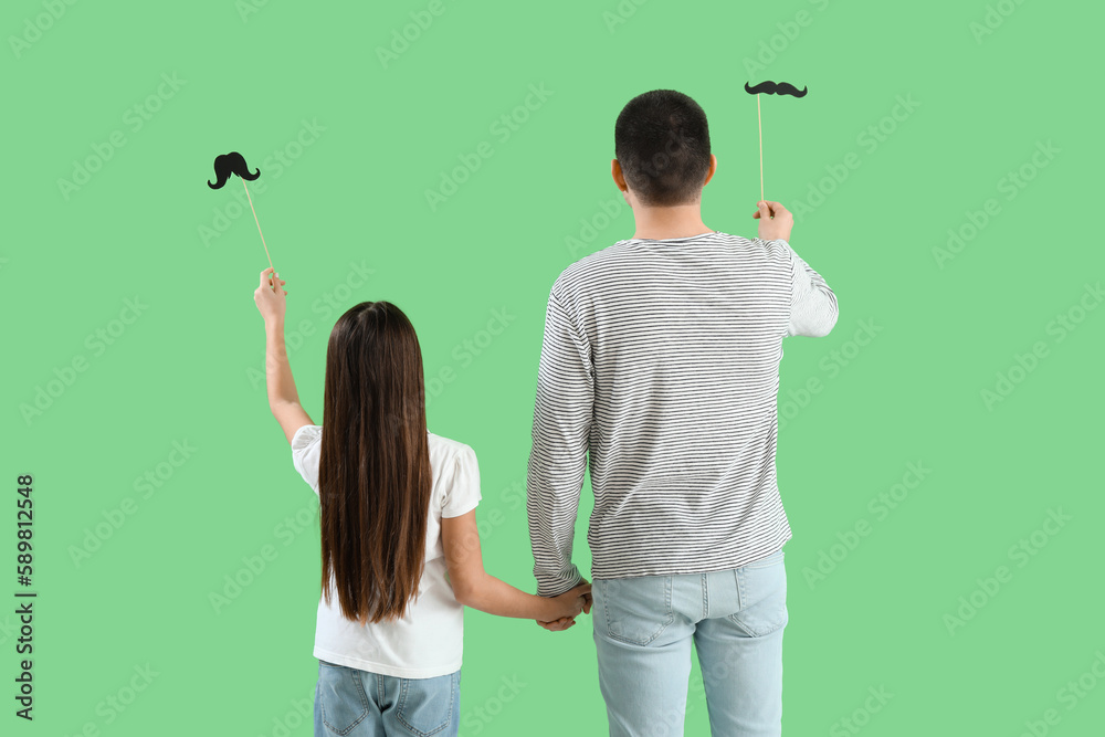 Father and his little daughter with paper mustache on green background, back view