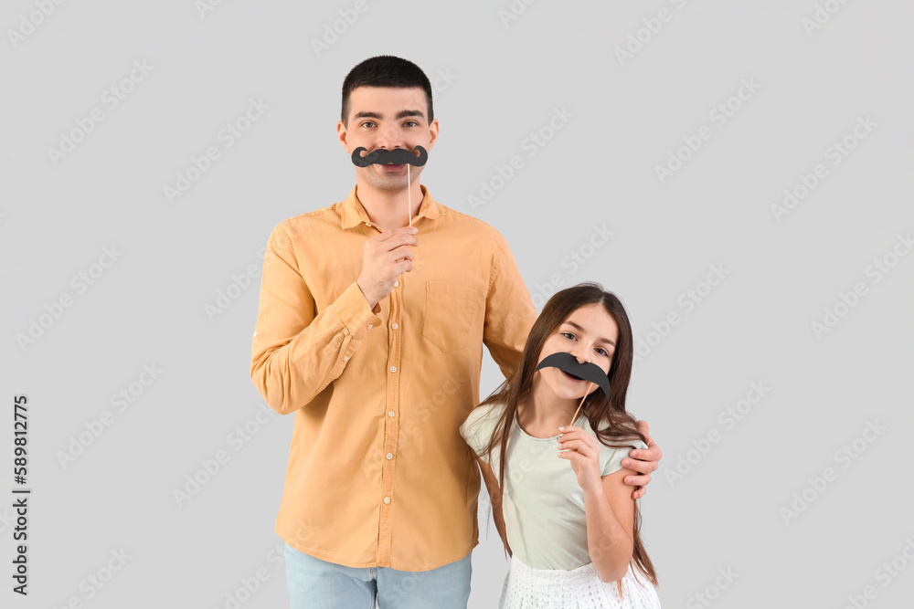 Portrait of father and his little daughter with paper mustache on light background