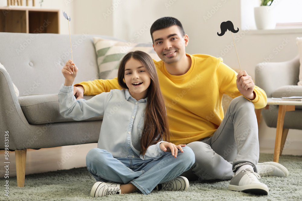 Portrait of father and his little daughter with paper mustache at home