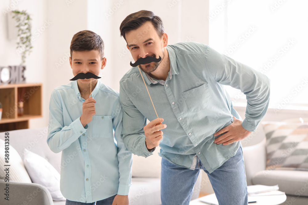 Portrait of father and his little son with paper mustache at home