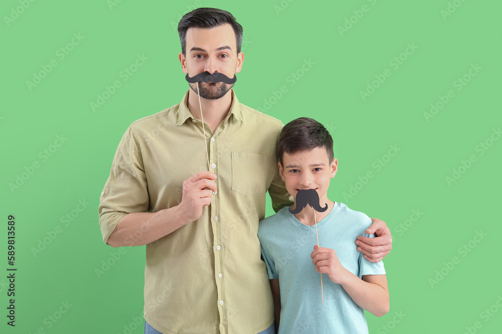 Portrait of father and his little son with paper mustache on green background