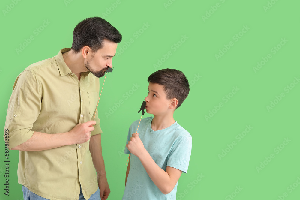 Portrait of father and his little son with paper mustache on green background