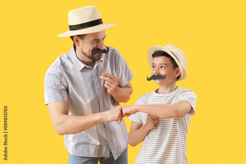 Portrait of father and his little son with paper mustache bumping fists on yellow background