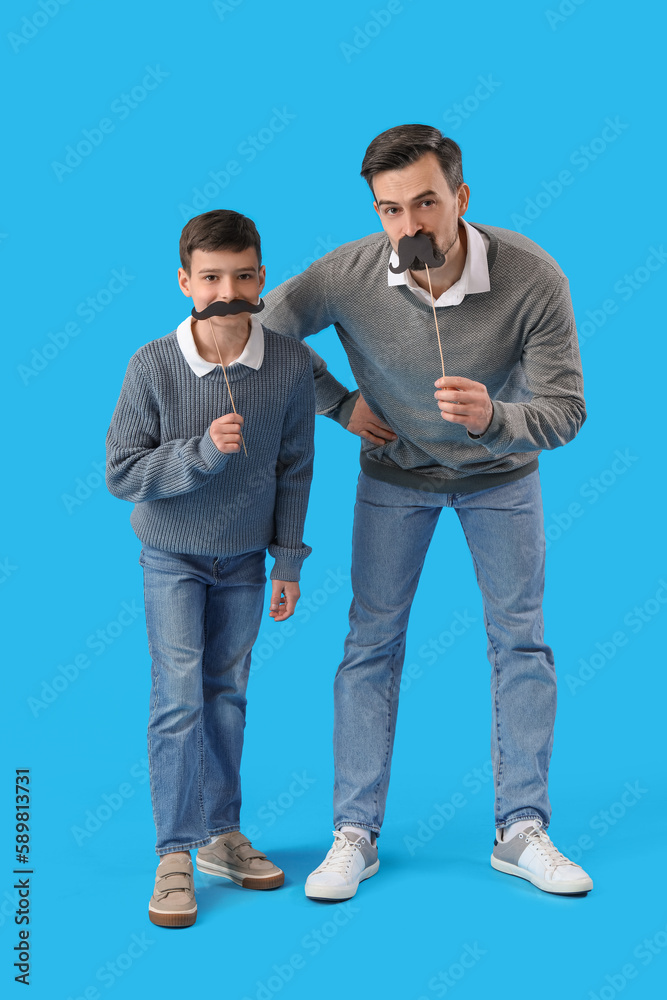 Portrait of father and his little son with paper mustache on light blue background