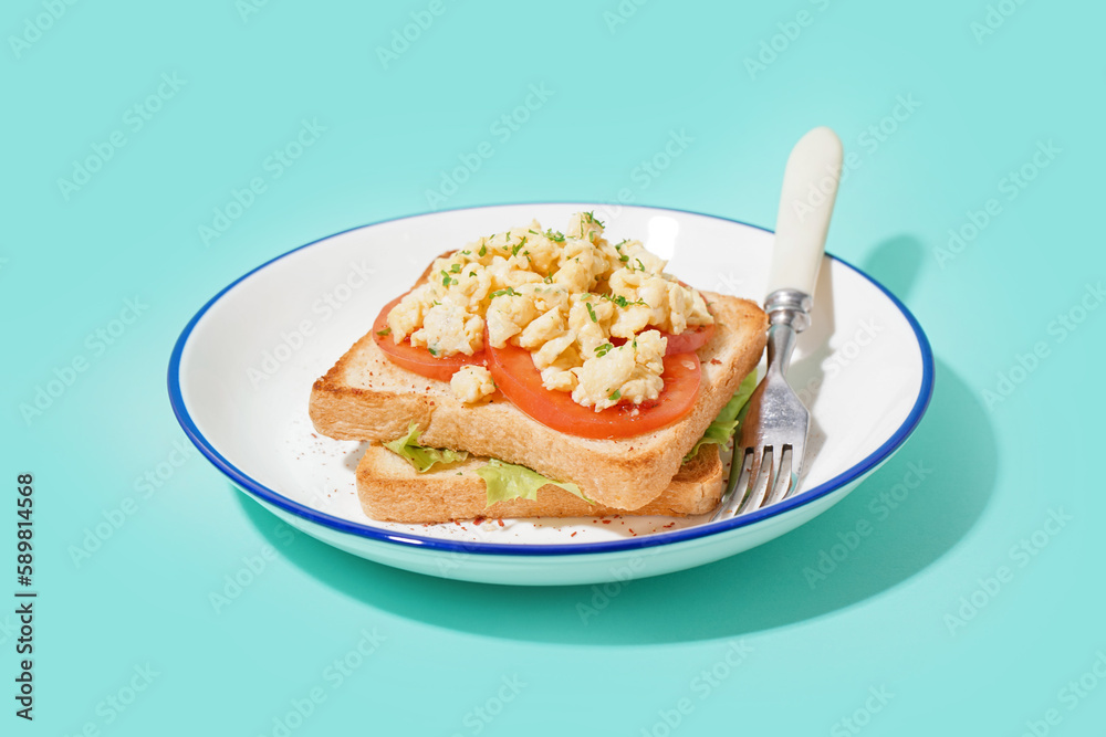 Plate with tasty scrambled eggs sandwich on blue background