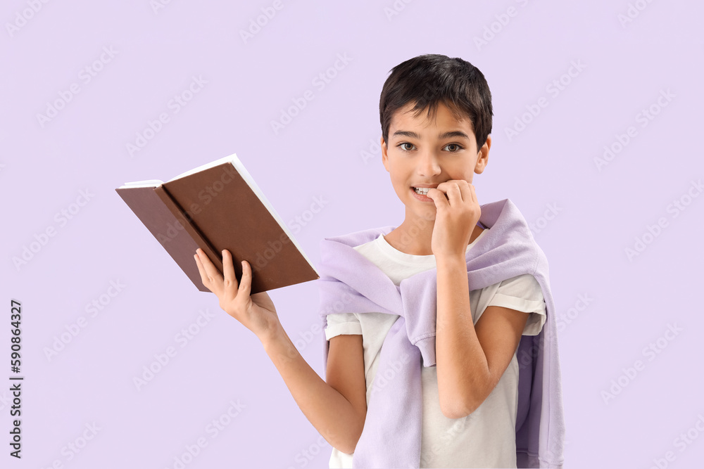 Little boy with book biting nails on lilac background