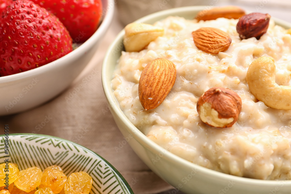 Bowls with tasty oatmeal, nuts, strawberries and raisins on grey wooden background