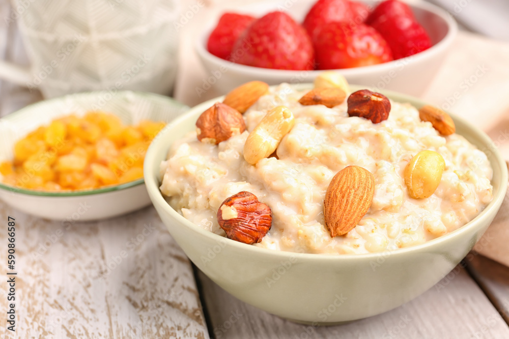 Bowls with tasty oatmeal, nuts, strawberries and raisins on grey wooden background