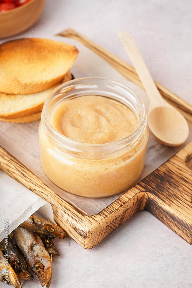 Wooden board with jar of caviar and fried baguette pieces on grey background