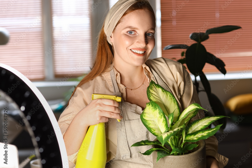 Female blogger with spray bottle and houseplant taking video at home