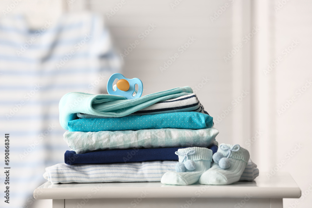 Stack of baby clothes and pacifier on table in room, closeup