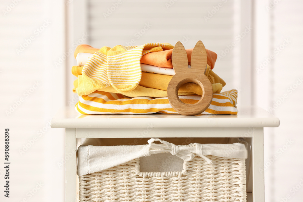 Stack of baby clothes and wooden toy on shelf unit against folding screen