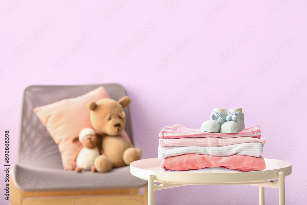 Stack of baby clothes and socks on table against color wall