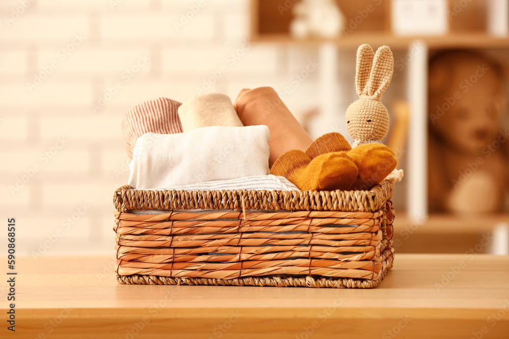 Basket with baby clothes and toy on wooden table